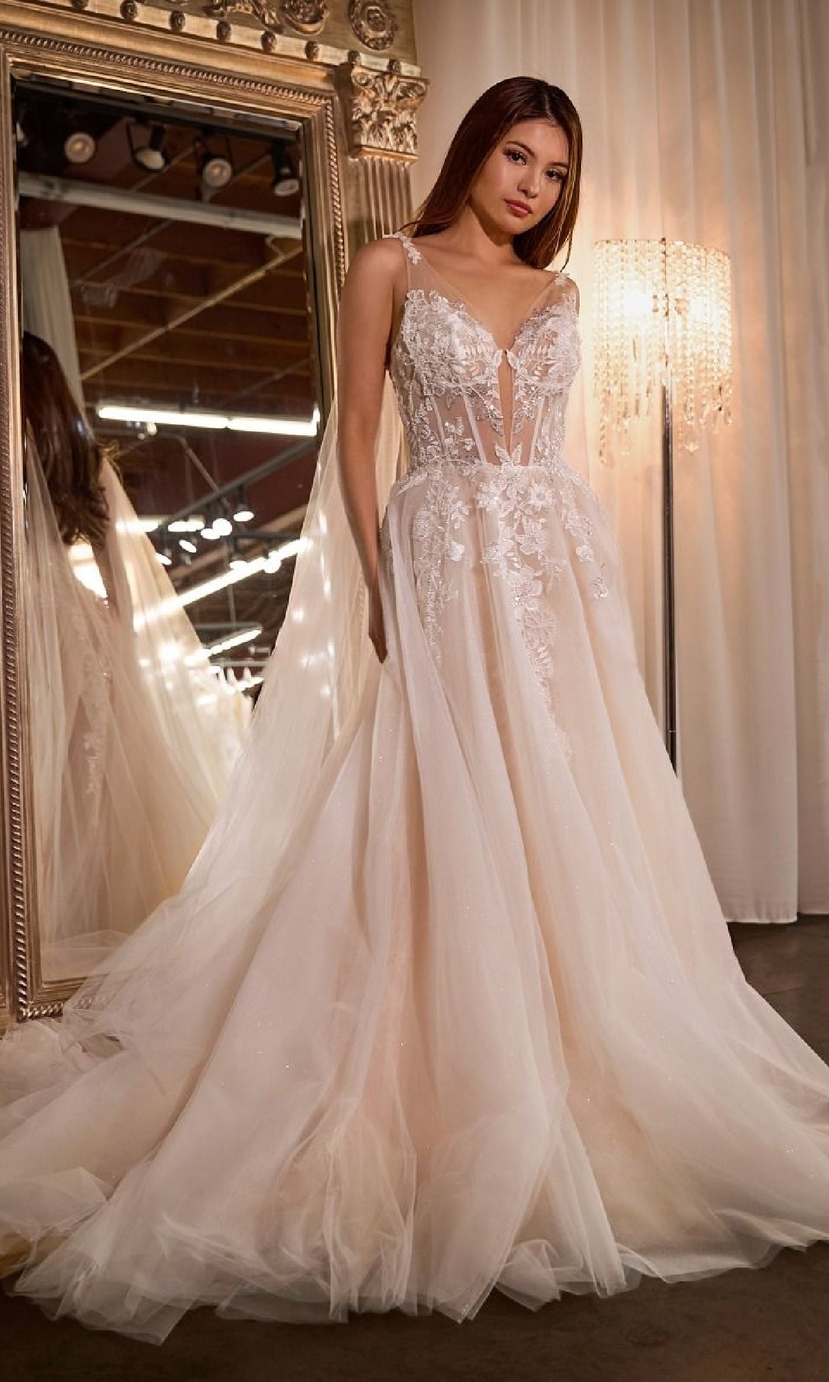 A woman stands before a large ornate mirror wearing the Ladivine CDS476W long wedding dress, featuring delicate floral lace detailing and a sweeping floor-length tulle skirt.